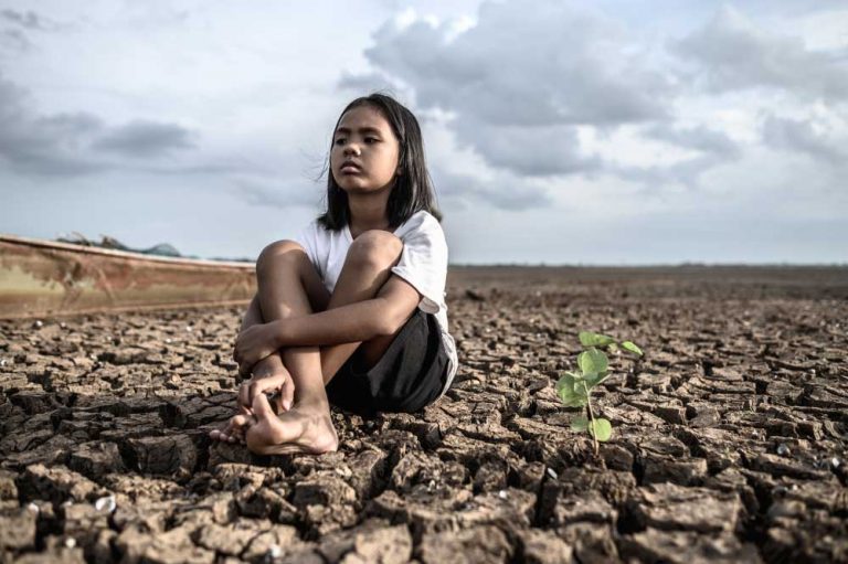 girls sitting hugging their knees looking sky having trees dry ground